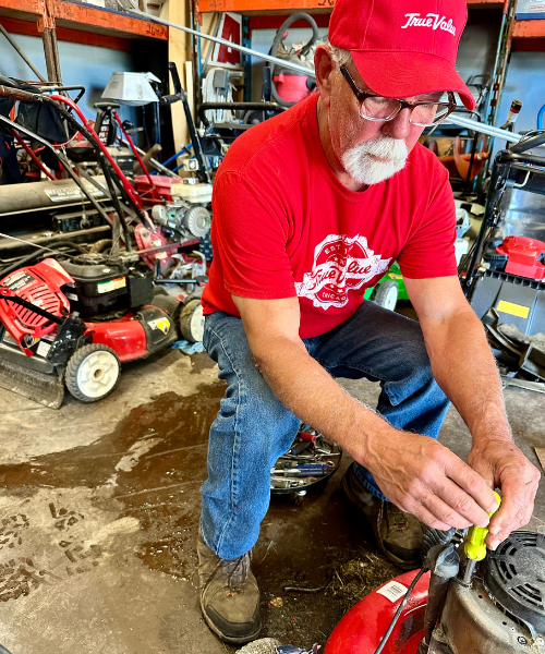 Fiore Rental employee using a yellow screwdriver on a push mower engine